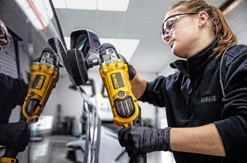 Personne utilise une polisseuse jaune DEWALT DWP849X sur un rétroviseur de voiture. Visage flouté.
