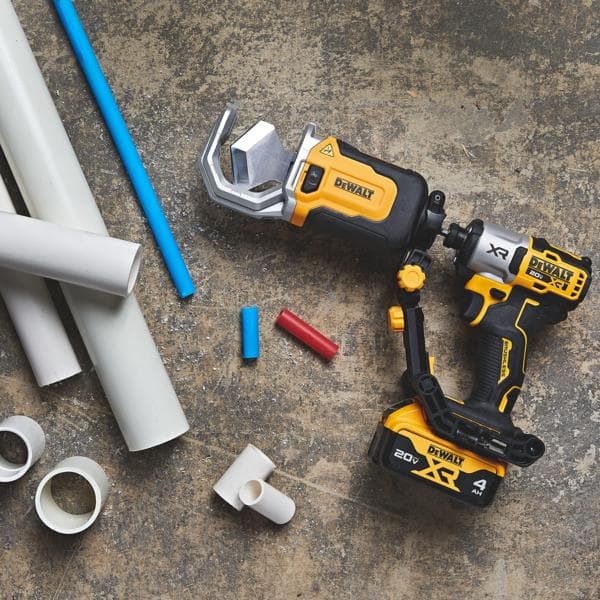 Un outil électrique sans fil DEWALT conçu pour couper des tuyaux en PVC, présenté sur une surface en béton à côté de plusieurs tuyaux et raccords de couleur blanche et colorée.