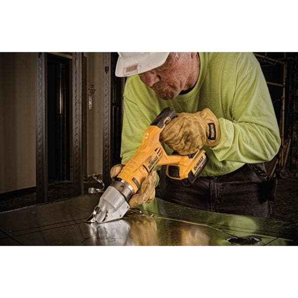 Un ouvrier portant un casque et des gants utilise un outil à cisaille métallique sans fil jaune DEWALT pour couper une tôle.