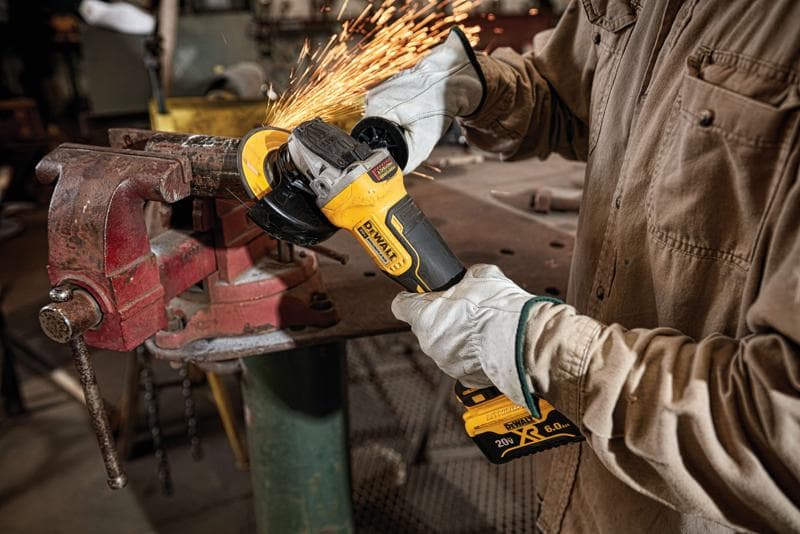Personne portant des gants de protection utilisant une meuleuse d’angle sans fil DEWALT, modèle DCG413R2, pour couper ou meuler du métal fixé dans un étau, avec des étincelles dans un atelier.