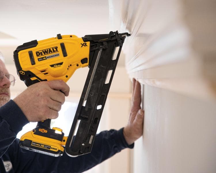 Une personne utilise un cloueur sans fil DEWALT 20V XR brushless pour fixer une moulure sur un mur.