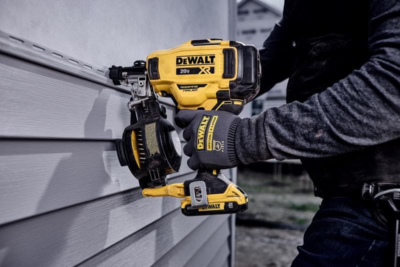 Une personne portant des gants utilise une cloueuse pour toiture sans fil DEWALT 20V XR pour fixer un revêtement sur un mur. L'outil est jaune et noir avec le logo DEWALT bien visible.