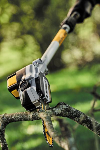 Gros plan sur une scie sur perche DEWALT coupant une branche d'arbre en extérieur, montrant la lame de la scie en train de découper la branche avec un arrière-plan vert flou.