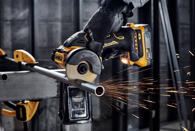 Une personne portant des gants utilise une meuleuse angulaire sans fil brushless DEWALT pour couper un tuyau en métal, produisant des étincelles dans un atelier industriel.