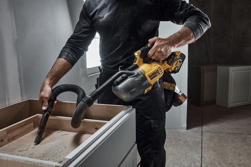 Une personne utilise un aspirateur portable sans fil DEWALT pour enlever de la sciure d’un tiroir de meuble dans un atelier ou un environnement de construction.