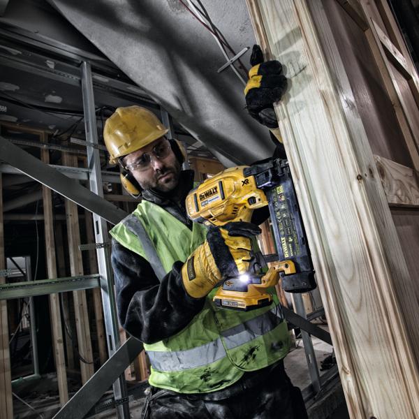 Ouvrier utilise un cloueur DEWALT DCN680 sur une charpente en bois, équipé de protections de sécurité.