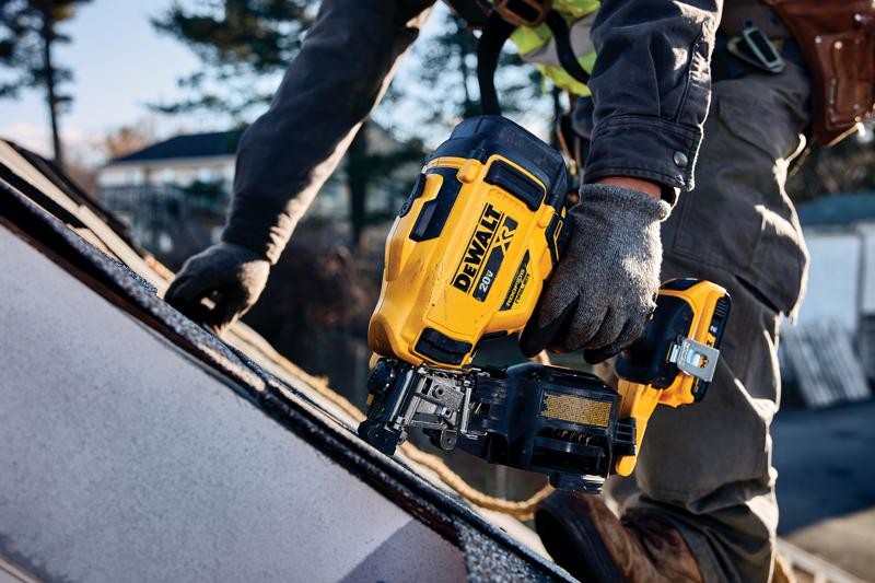 Une personne portant des gants de travail utilise un cloueur sans fil jaune DEWALT pour toiture sur un toit en pente à l'extérieur.