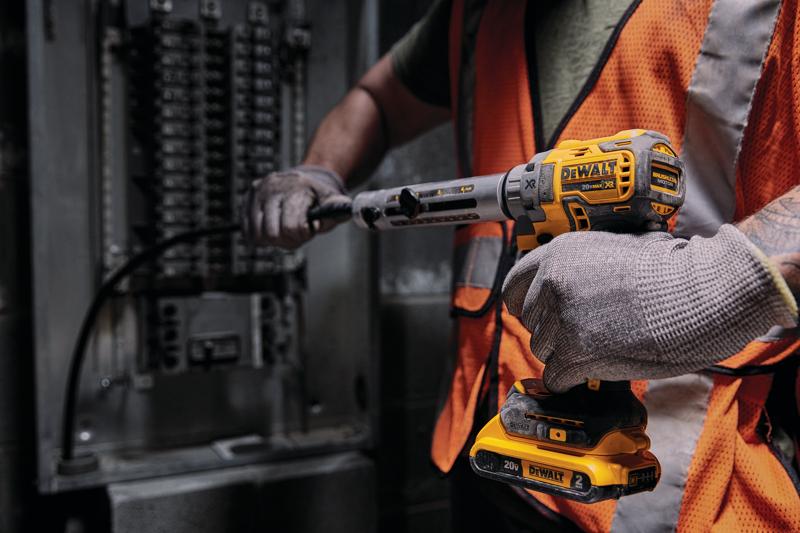 Une personne portant des gants et un gilet de sécurité orange utilise un outil électrique sans fil DEWALT 20V pour travailler sur un panneau électrique.