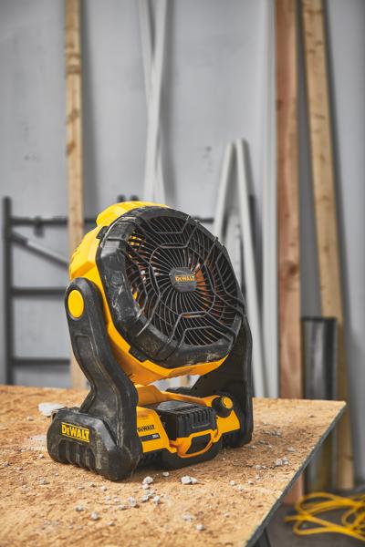 Un ventilateur portable sans fil DEWALT (modèle DCE512B) est posé sur un établi en bois dans un atelier avec des matériaux de construction en arrière-plan.
