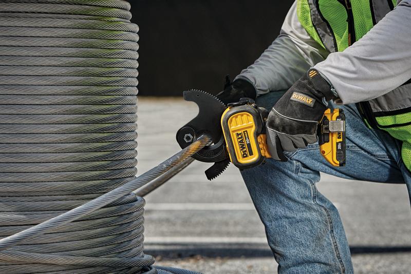 Une personne portant des gants de sécurité et un gilet de sécurité utilise un outil électrique sans fil DEWALT pour couper un câble métallique épais à côté d'une grande bobine de fil en extérieur.