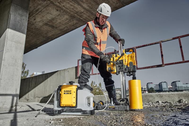 Ouvrier utilisant une carotteuse DEWALT DCPS151 sur béton, casque et gilet de sécurité au chantier.