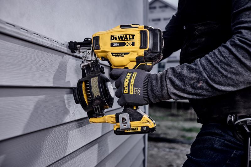 Une personne portant des gants utilise une cloueuse pour toiture sans fil DEWALT 20V XR pour fixer un revêtement sur un mur. L'outil est jaune et noir avec le logo DEWALT bien visible.