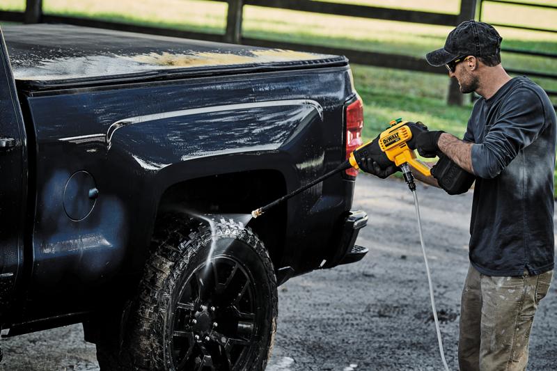 Une personne utilise un laveur à pression sans fil DEWALT DCPW550B pour nettoyer la roue et le côté d'un pick-up noir à l'extérieur.